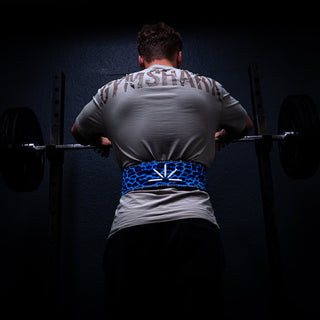 Man with blue Trackfie lifting belt standing in front of a squat rack with hands on a barbell