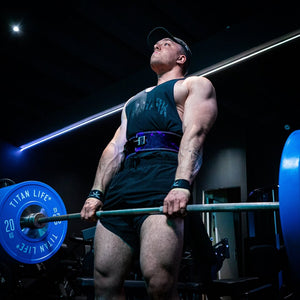 A man deadlifting heavy weight and using lifting straps and a purple lifting belt in a gym
