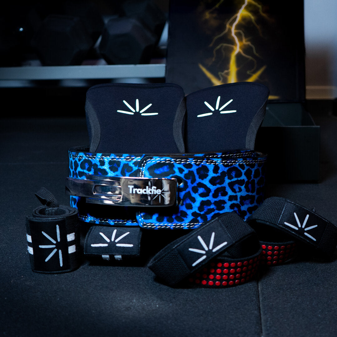 Blue leopard Trackfie bundle consisting of lever belt, knee sleeves, wrist wraps, and lifting straps assembled in a gym