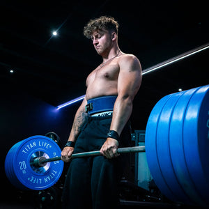 Man deadlifting in a gym with blue lever belt and lifting straps