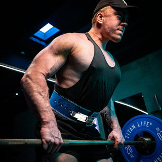 Man performing barbell rows exercise with blue lever belt in a gym