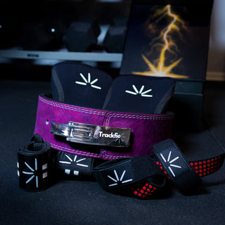 Purple Trackfie bundle with purple lever belt, black knee sleeves, wrist wraps, and lifting straps assembled in a gym