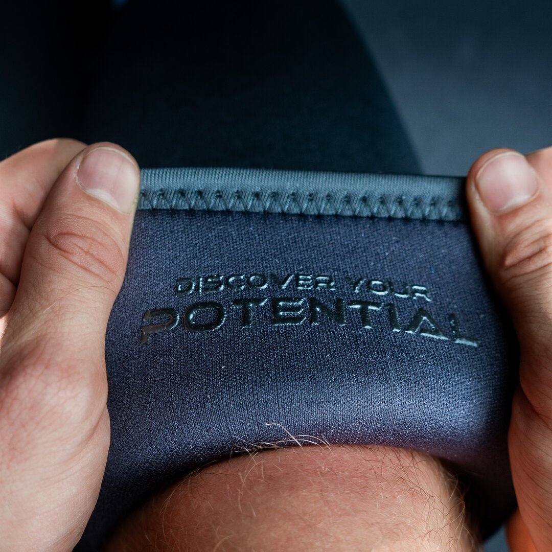 Black Unlisted Strength knee sleeves being applied to legs with 'discover your potential' text on the inside