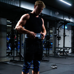 Man bluckeling a blue Unlisted Strength lifting belt and wearing blue knee sleeves in a gym
