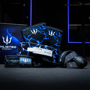 Blue Unlisted Strength bundle consisting of lever belt, knee sleeves, wrist wraps, and lifting straps assembled in front of an Unlisted Strength box in a gym