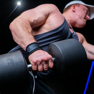 A man with black lifting straps standing in the gym lifting heavy dumbbell