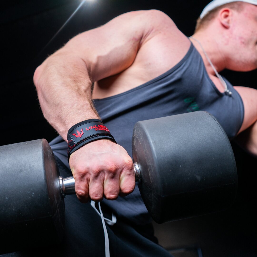 A man with red lifting straps in the gym lifting a heavy dumbbell