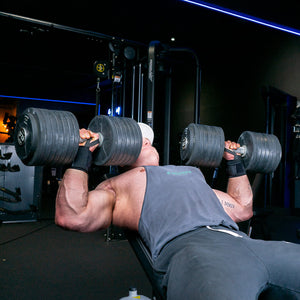 Man performing incline dumbbell press exercise with black wrist wraps in the gym