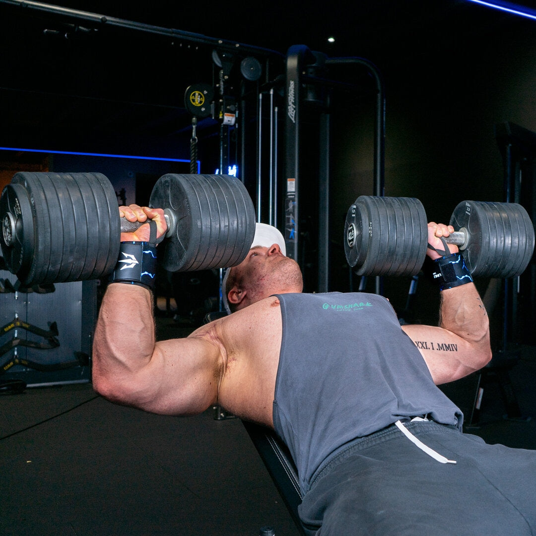 Man performing incline dumbbell press exercise with blue wrist wraps in the gym